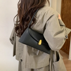 Close-up of a retro black leather shoulder bag with a gold buckle on a trench coat model