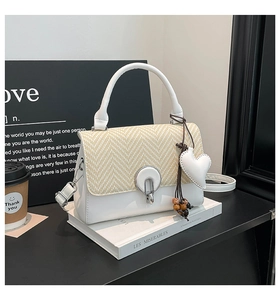 Detalle del bolso de cuero blanco con solapa trenzada y colgante de corazón con cuentas de madera