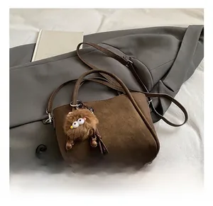 Detail of dark brown suede bucket bag with a cute plush monster charm and strap