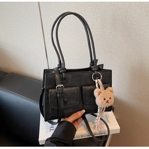 Close-up of black matte shoulder bag with knot handles and cute plush bear charm decoration