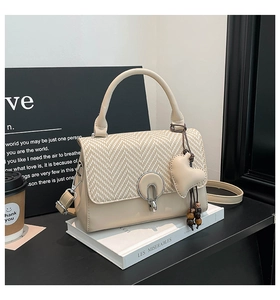 Detalle de bolso beige con solapa de tejido y colgante de corazón con cuentas de madera