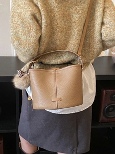 Classic brown pebble leather bucket bag with plush charm on a female model