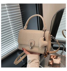 Detalle de bolso beige con diseño de pata de gallo, amuleto corazón y cuentas madera