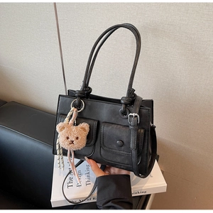Detail of black PU leather tote bag with two front pockets and plush bear charm decor