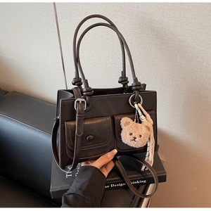 Detailed view of deep brown leather bucket bag with front flap pockets and bear charm