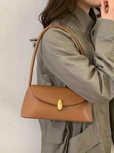Minimalist caramel brown leather shoulder bag with gold buckle on trench coat