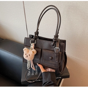 Detail of dark brown faux leather tote bag with functional pockets and plush bear charm