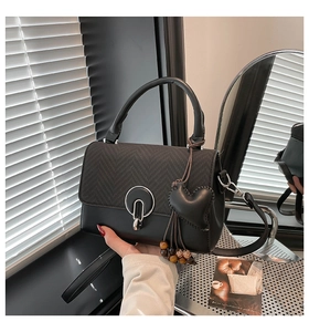 Detalle de bolso bandolera negro con hebilla en U y colgante de cuentas de corazón