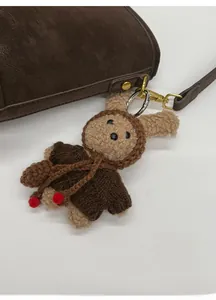 Close-up of a plush bear keychain with a brown knit sweater hanging on a leather bag