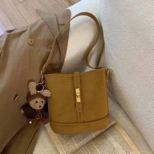 Detail of mustard yellow matte bucket bag with golden lock and cute rabbit charm accessory