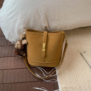 Detail of yellow bucket bag featuring golden twist lock and cute bear charm on a rug