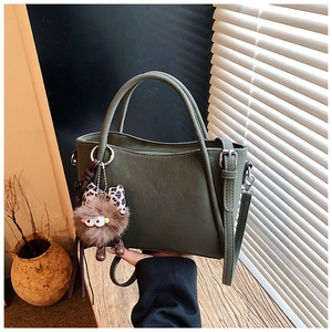 Detail of dark green matte crossbody bag with unique brown plush monster charm and silver hardware