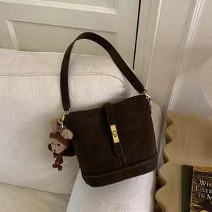 Macro shot of dark brown matte bucket bag with golden twist lock and plush bear charm
