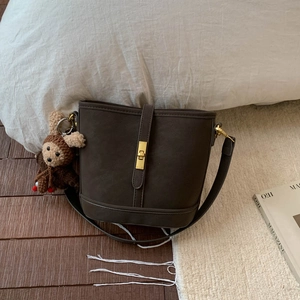 Detail of dark brown matte bucket bag with golden buckle and cute bear pendant charm