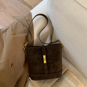 Detail of vintage brown suede bucket bag with gold clasp on a minimalist sofa