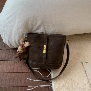 Detail of dark brown bucket bag featuring a gold twist lock and a cute bear plush pendant