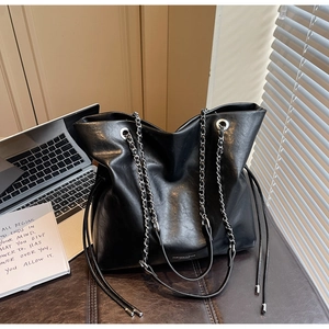 Macro detail of black leather tote bag with silver chain strap and side cord detail