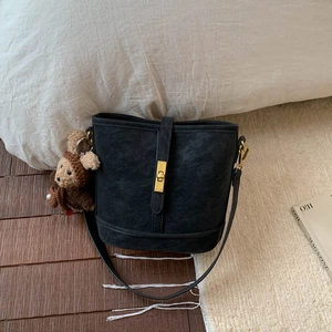 Detail of black matte bucket bag featuring a gold clasp and a cute brown bear charm