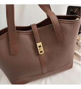 Close-up of brown pebbled leather tote bag featuring a polished gold rectangular metal lock