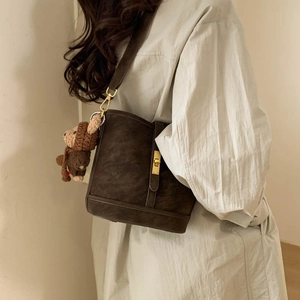 Detail of vintage brown bucket bag with gold lock and cute knitted bear charm