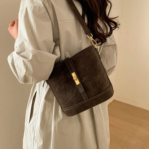 Detail of vintage matte bucket bag with golden lock shown on model in minimalist interior