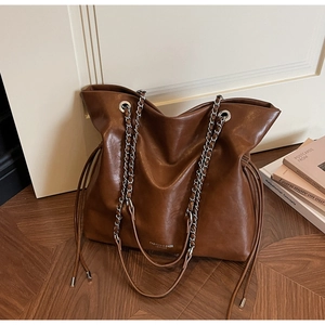 Detail of caramel brown leather tote bag with chain strap and drawstring accents