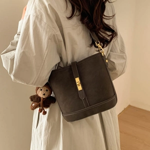 Detail of vintage matte bucket bag with golden buckle and cute knitted bear charm