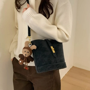Detail of black matte bucket bag with gold clasp and brown knitted bunny charm