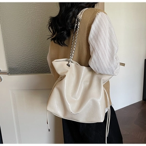 Detail of cream drawstring tote with silver chain strap on a model shoulder