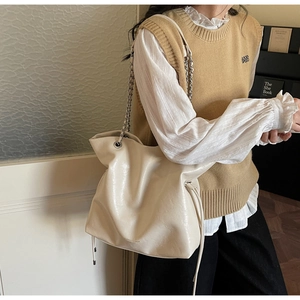 Detailed close-up of large beige leather tote bag with metal chain and fashion text