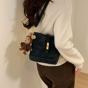 Detail of black matte bucket bag featuring a gold buckle and teddy bear charm on model