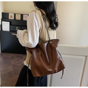 Macro detail of the brown leather tote bag showing metal chain strap and side drawstring