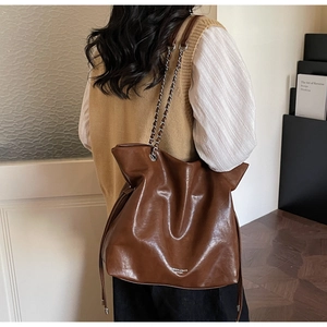 Detail of a dark brown leather tote bag with metal chain strap and side drawstring texture