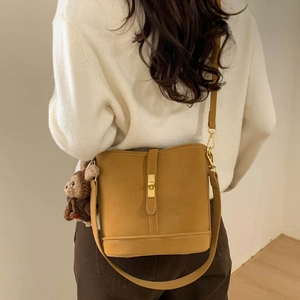 Rear view of a model wearing the brown bucket bag with a plush bear charm and gold lock