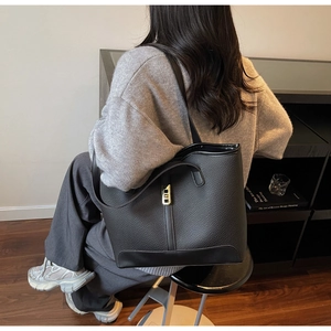 Detail of black lychee texture leather tote bag with gold buckle on a shoulder model