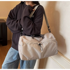 Close-up of beige travel bag with plaid pocket, drawstrings and adjustable strap