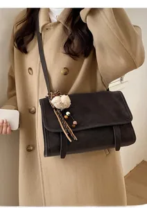 Detail of vintage brown messenger bag with plush charm and striped strap on camel coat