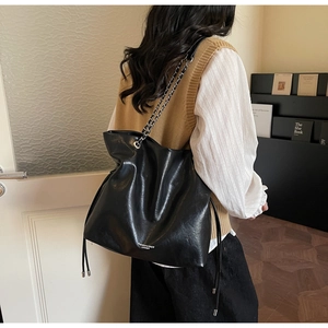 Detail of black glossy leather bucket bag showing textured finish and chain strap