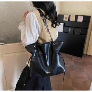 Detail of black leather tote bag featuring a silver chain strap and side drawstring design