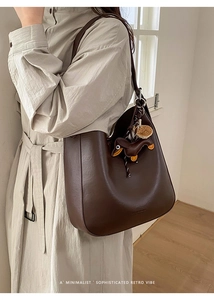 Detail of dark brown leather tote bag with unique dachshund charm on beige coat
