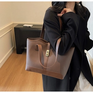 Detail of a large brown pebble leather tote bag with a golden metal lock closure