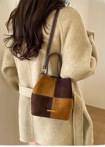 Detail of color-block suede bucket bag with contrast stitching and golden nameplate
