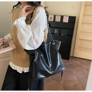 Detail view of large black leather tote bag featuring chain straps and side drawstring