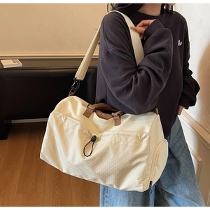 Detailed macro of cream travel bag showing quilted texture and letter embroidery