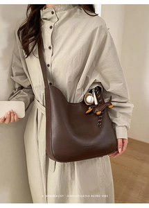 Detail of dark brown leather hobo bag with a wide strap and decorative charms