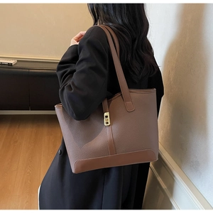 Detail of a brown textured leather tote bag featuring a gold metal lock and shoulder strap