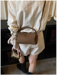 Brown litchi grain leather barrel bag with plush bunny charm shown on model back