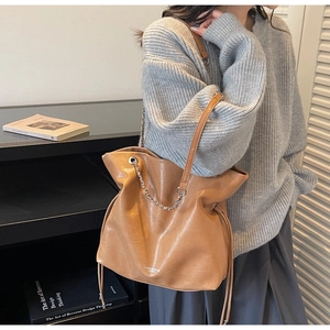 Macro detail of tan leather bucket bag featuring drawstring closure and silver chain strap