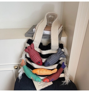 Detail of striped knit tote bag featuring colorful fish charms and white feather tassels