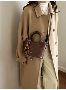 Detail of dark brown leather tote with ethnic bead charm and adjustable strap worn on coat